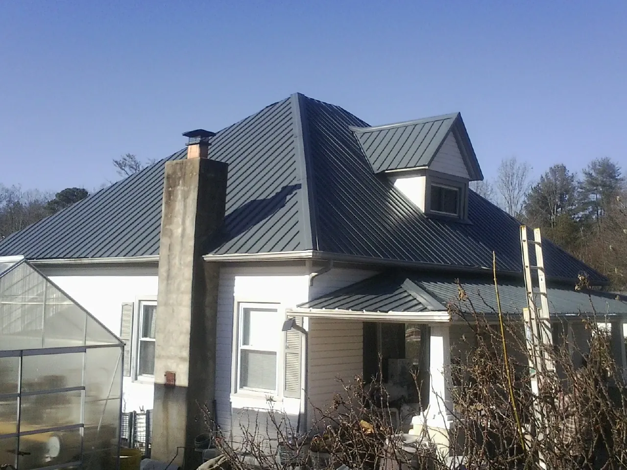 Dark blue standing seam metal roof on a white farmhouse with dormer — Slate & Tile Roof Repair by Roofing Brothers in Carmichaels