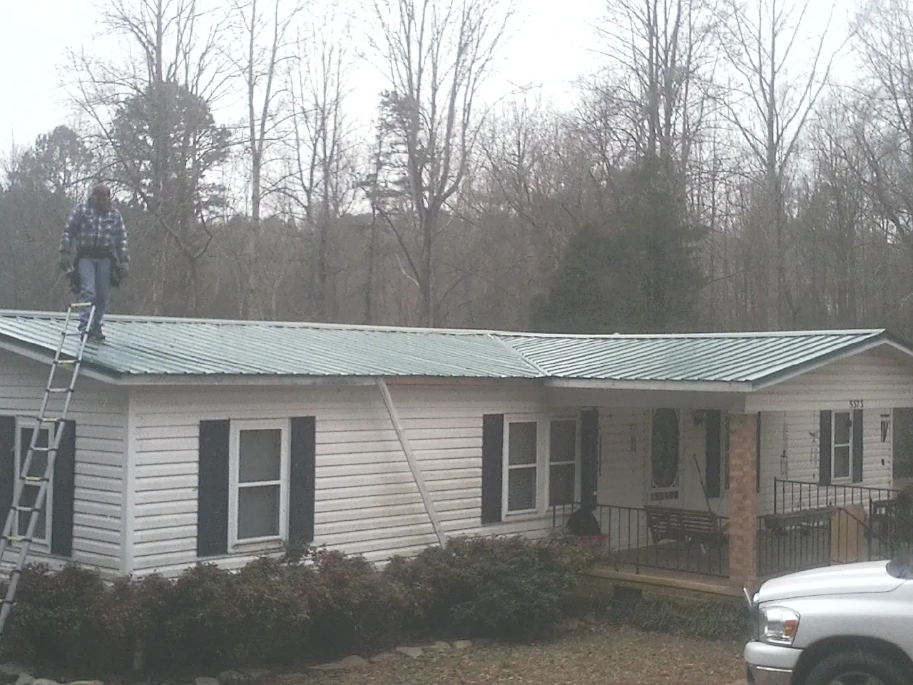 Worker on a ladder beside a new green metal roof on a ranch home in Carmichaels