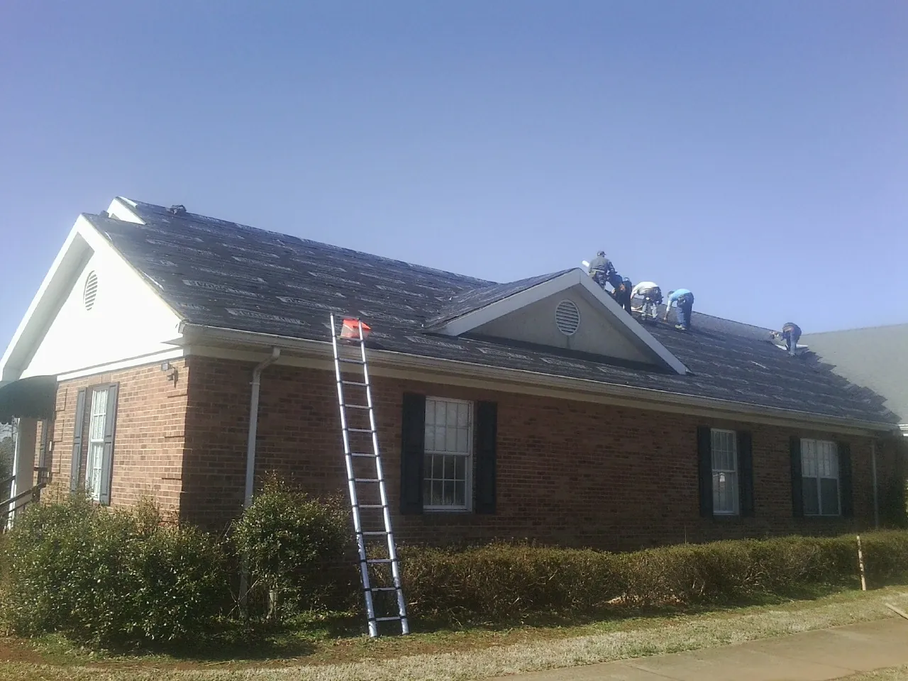 Crew tearing shingles off a brick ranch roof with a ladder set — Emergency Roof Repair work by our crew in Carmichaels