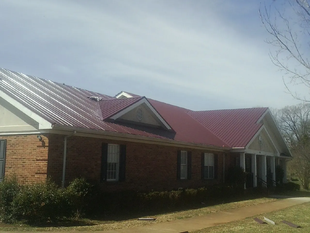 Red metal roof with gabled entries on a long brick building, from a Hail Damage Roof Repair job in Carmichaels