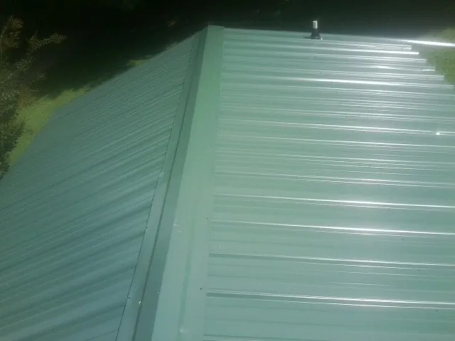 New green metal panels meeting at the ridge of a roof — Flat Roof Repair work by our crew in Carmichaels