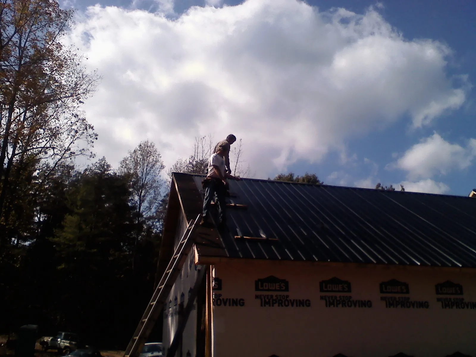 Roofer fastening dark metal panels high against a cloudy sky, from a Roof Inspection job in Carmichaels