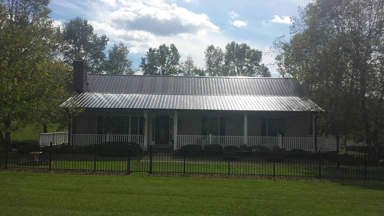 Gray metal roof on a brick ranch with a full width front porch — Gutter Guard Installation work by our crew in Carmichaels