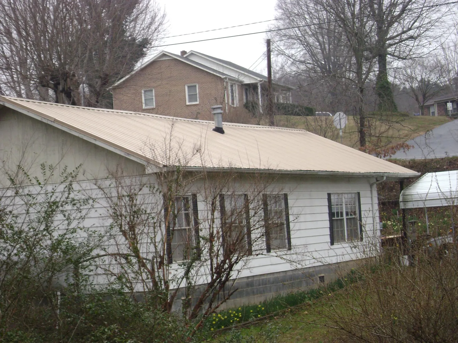 Tan metal roof on a white sided house set into a hillside — Commercial Roofing by Roofing Brothers in Carmichaels